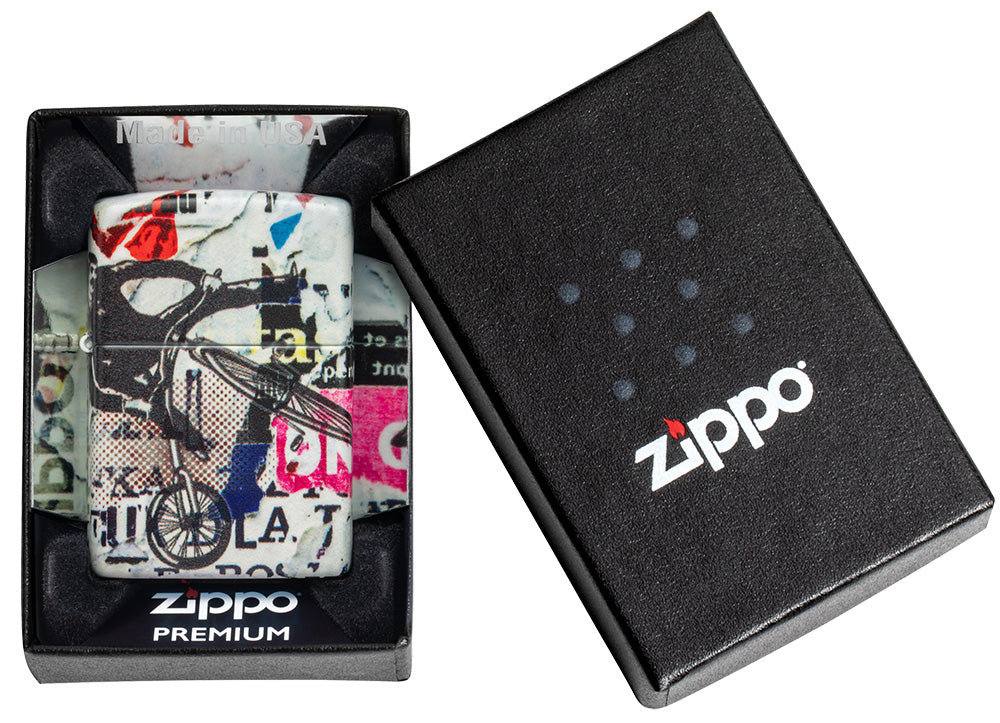 Briquet Zippo 540° vue de face dans le coffret cadeau et fait de métal, avec une illustration en couleur inspiré de l'art de la rue, qui montre un cycliste téméraire au-dessus d'un collage d'autocollants et de tracts.