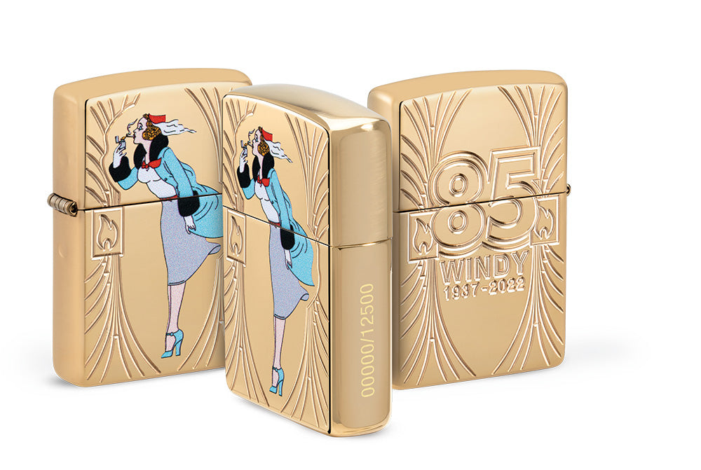 Briquet Zippo de face, de l'arrière et de côté couleur dorée et fait de métal, avec une illustration en couleur qui montre Windy, notre modèle publicitaire préféré pour célébrer les 85 ans de Zippo