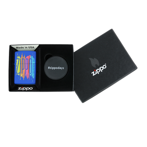 Briquet Zippo vue de face BLEU MATTE dans le coffret cadeau et fait de métal, avec une illustration en couleur qui montre le logo de Zippo teinté avec des couleurs de peinture.