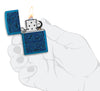 Briquet Zippo vue de face ouverte et allumée en bleu brillant avec illustration de créatures marines dans le style de l'art aborigène en main stylisée