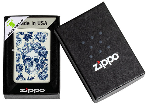 Briquet Zippo brille dans le noir Tête de mort avec couronne entourée de fleurs bleues dans une boîte ouverte