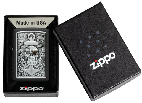 Briquet Zippo vue de face dans le coffret cadeau emblème et fait de métal, avec une illustration en couleur qui montre le motif classique du crâne et des os croisés