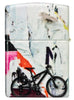 Briquet Zippo 540° vue de l'arrière et fait de métal, avec une illustration en couleur inspiré de l'art de la rue, qui montre un cycliste téméraire au-dessus d'un collage d'autocollants et de tracts.