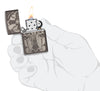 Briquet Zippo vue de face en main stylisée ouvert et allumé fait de métal, avec une illustration en couleur qui montre un motif de tête de mort et de croix tout droit