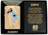 Briquet Zippo vue de face dans le coffret cadeau en couleur dorée et fait de métal, avec une illustration gravée en couleur qui montre Windy, notre modèle publicitaire préféré pour célébrer les 85 ans de Zippo