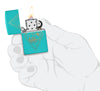 Briquet Flat Zippo vue de face Turquoise en main stylisée  ouvert et allumé et fait de métal, avec une illustration en couleur qui montre un motif bohémien outdoor gravé au laser.