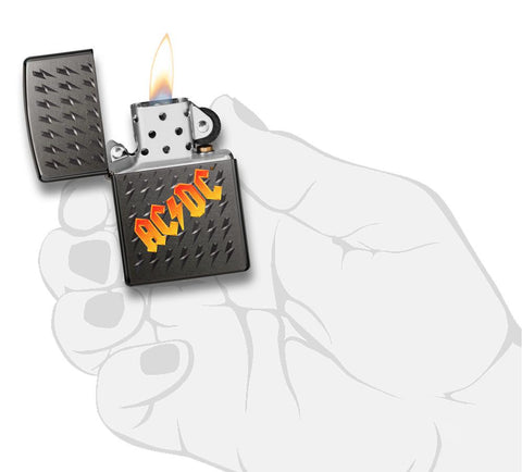 Vue de face briquet Zippo Black Ice avec logo AC/DC et petits éclairs gravés, ouvert avec flamme dans une main stylisée