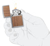 Vue de face briquet Zippo chrome brossé avec emblème Woodchuck, ouvert avec flamme dans une main stylisée 