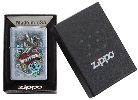 Briquet Zippo chromé style tatouage avec cœur, hirondelle et bannière Zippo, dans une boîte ouverte