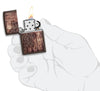 Briquet Zippo motif mandala marron clair sur arrière-plan en bois, ouvert avec flamme dans une main stylisée