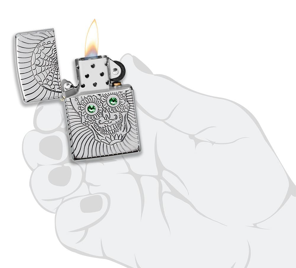 Briquet Zippo avec gravure profonde tête de mort et yeux en éléMen,ts Swarovski, ouvert avec flamme dans une main stylisée