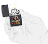Briquet Zippo noir mat avec tête de mort multicolore, ouvert avec flamme dans une main stylisée