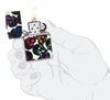 Briquet Zippo 540° vue de face ouvert et allumé Skulls Design avec quelques têtes de mort multicolores brillant dans la nuit en main stylisée