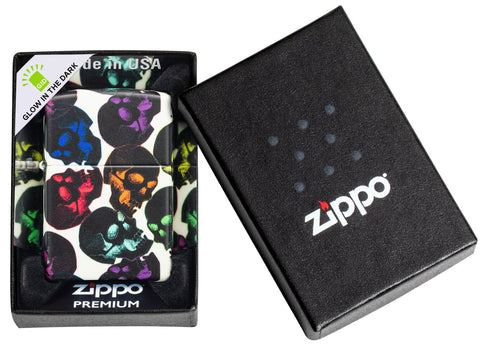 Briquet Zippo 540° vue de face Skulls Design avec quelques crânes multicolores qui brillent dans la nuit dans sa boîte noire de qualité supérieure.