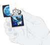 Briquet Zippo vue de face en main stylisée ouvert et allumé fait de métal, avec une illustration en couleur qui montre l'impression d'un corbeau noir au clair de lune sur un crâne sur fond noir mat.